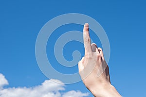 Close-up female hand with index finger up on a background of blue sky with clouds, copy space