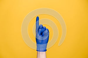 Close up of female hand in medical protective gloves showing no, isolated on yellow background with copy space for advertisement