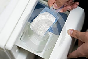 Close up female hand pour the washing powder detergent into machine d