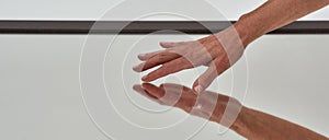 Close up of female hand reaching to touch mirror reflective surface on the floor isolated over light background