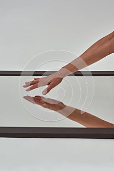 Close up of female hand reaching to touch mirror reflective surface on the floor isolated over light background