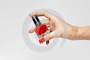 Close-up of female hand with red manicure holding a glitter nail polish of red color on white background
