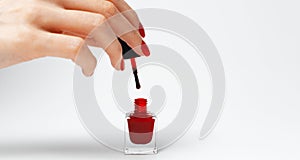 Close-up of female hand with red manicure holding a glitter nail polish of red color on white background