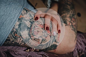 Close up female hand with red nails holding strong man hand with scarry tattoo