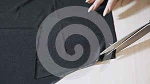 Close up female hand with the scissors cutting the black fabric.