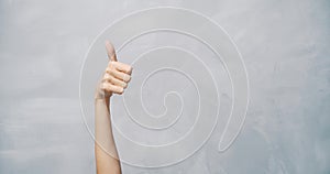 Close-up of female hand showing thumb up on a grey background. Copy space