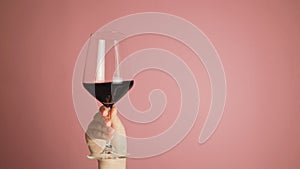 Close up female hand swirling red wine in wine glass. Wine expert tasting, rating and drinking wine on pink wall studio