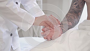 Close-up of female hand taking pulse of unrecognizable Caucasian man with tattoos on hand. Doctor doing medical