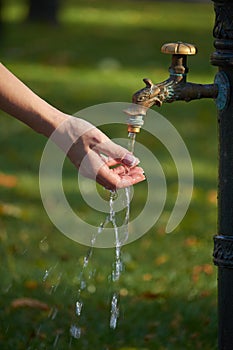 Close-up of female hand under water from an old-style column with drinking water in an autumn park, selective focus