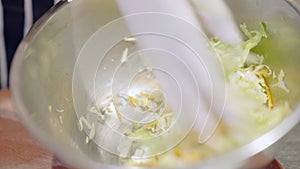 Close-up of female hand in white glove mixing healthful vegetable salad in metal bowl. Unrecognizable cook working in