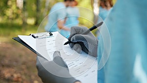 Close-up of female hand writing volunteer report in forest during clean-up work