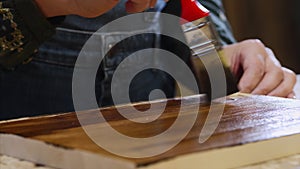 Close-up of female hands is applying of protective varnish on wood plank.