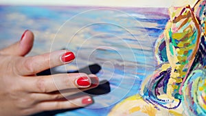 Close-up, female hands of the artist with bright red manicure . she applies paint to the canvas with her fingers, using