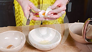 Close-up of female hands breaking eggshells and dividing yolks and whites into different bowls. Cooking biscuit or dough