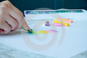 Close-up of female hands are drawing with multicolored chalks on a white sheet, a box with crayons