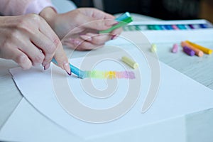 Close-up of female hands are drawing with multicolored chalks on a white sheet, a box with crayons