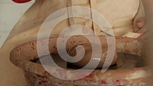 Close-up female hands dropping water on raw clay on pottery wheel