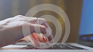 Close-up of female hands, a girl is typing on a laptop, and festive lights are flickering in the background