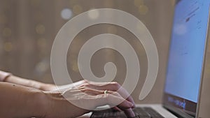 Close-up of female hands, a girl is typing on a laptop, and festive lights are flickering in the background