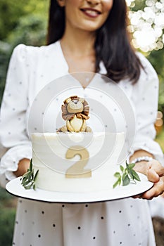 Close up of female hands hold a birthday baby cake. Delicious sweet pie with cute lion cub, number two and leaves photo