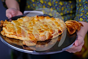 Close-up of female hands holding an appetizing baked cake on a metal tray, concept of festive dishes, made at home food