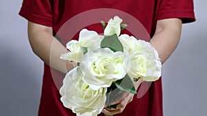 Close up female hands holding colorful roses bouquet. Woman hands touching rose buds leafs, white knitted sweater background