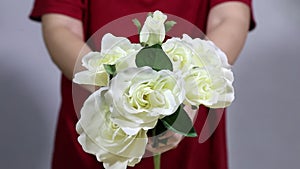 Close up female hands holding colorful roses bouquet. Woman hands touching rose buds leafs, white knitted sweater background