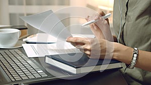 Close up of female hands holding a contract or financial report and taking notes at the workplace