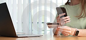 Close up female hands holding credit card and smartphone, young woman paying online, using banking service, entering