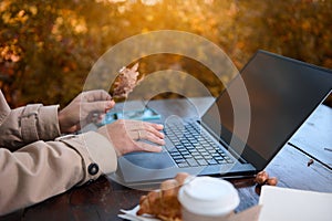 Close-up of female hands holding fallen oak leaf and typing on laptop keyboard while working remotely outdoors in countryside with