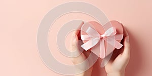Close up on female hands holding a gift in a pink heart presents for valentine day, birthday, mother\'s day.