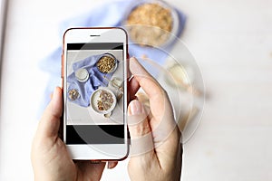 Close up of female hands holding mobile phone taking a picture of granola cereals, milk yogurt and trail mix vegetarian dieting br