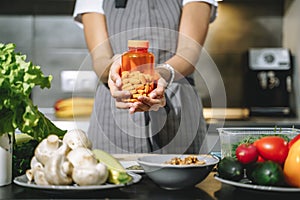 Close up of female hands holding nutritional supplements or vitamins in the kitchen. Choice, balanced diet and health concept