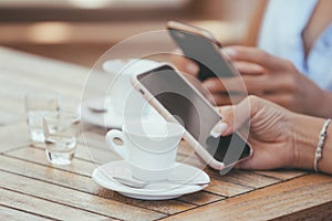 Close-up of female hands holding phones chatting on social network or shopping online in cafe with two cups of coffee photo