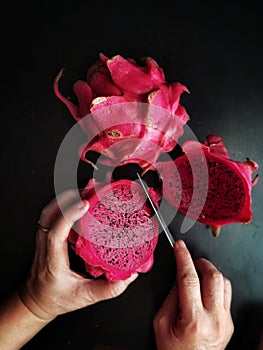 Close-up of female hands holding pink dragon fruit on black background