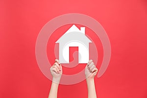 Close up of female hands holding small white paper house, isolated over red color background wall in studio with copy space for