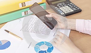 Close up female hands holding smart phone while connecting to wireless, businessman using technology sitting at wooden desk,