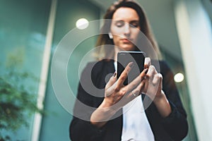 Close-up of female hands holding a smartphone in the evening on the street, focused businesswoman in a black suit using a mobile