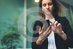 Close-up of female hands holding a smartphone  on the street, focused businesswoman in a black suit and using a modern smartphone