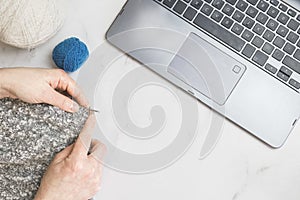 Close-up of female hands with knitting needles and knitting in front of a laptop