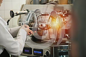 Close up of female hands making espresso with pressing ground coffee machine at coffee shop