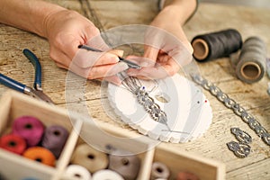 Close up of female hands making a macramÃ© bracelet with kumihimo on a wooden table with tools, spools of thread, natural stones