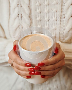 Close-up of female hands with a mug of beverage. Girl in warm sweater is holding hot cup of coffee or cocoa in hands.