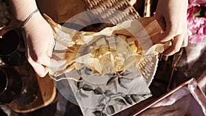 Close up of female hands open a small paper bag with cheese cut into cubes. Wine glasses. Picnic concept. Footage from