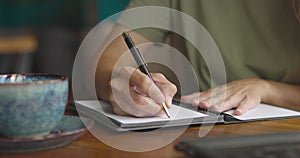 Close up of female hands opening paper notebook and taking notes.Woman working in a cozy cafe