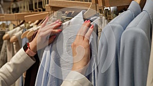 Close-up of Female Hands Plucked Hanger Choosing Clothes in a Clothing Store. The blonde's hand runs through the