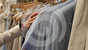 Close-up of Female Hands Plucked Hanger Choosing Clothes in a Clothing Store. The blonde's hand runs through the