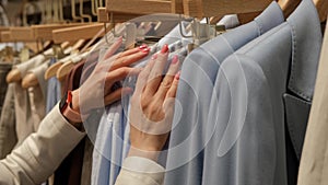 Close-up of Female Hands Plucked Hanger Choosing Clothes in a Clothing Store. The blonde's hand runs through the