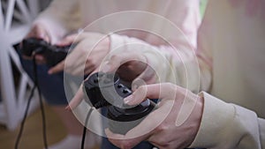 Close-up female hands pressing game controller buttons gaming with sibling. Two unrecognizable absorbed Caucasian twin