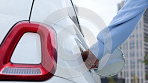 Close up of female hands putting charge cable into charging port in electric car outdoors in city. Woman driver charges